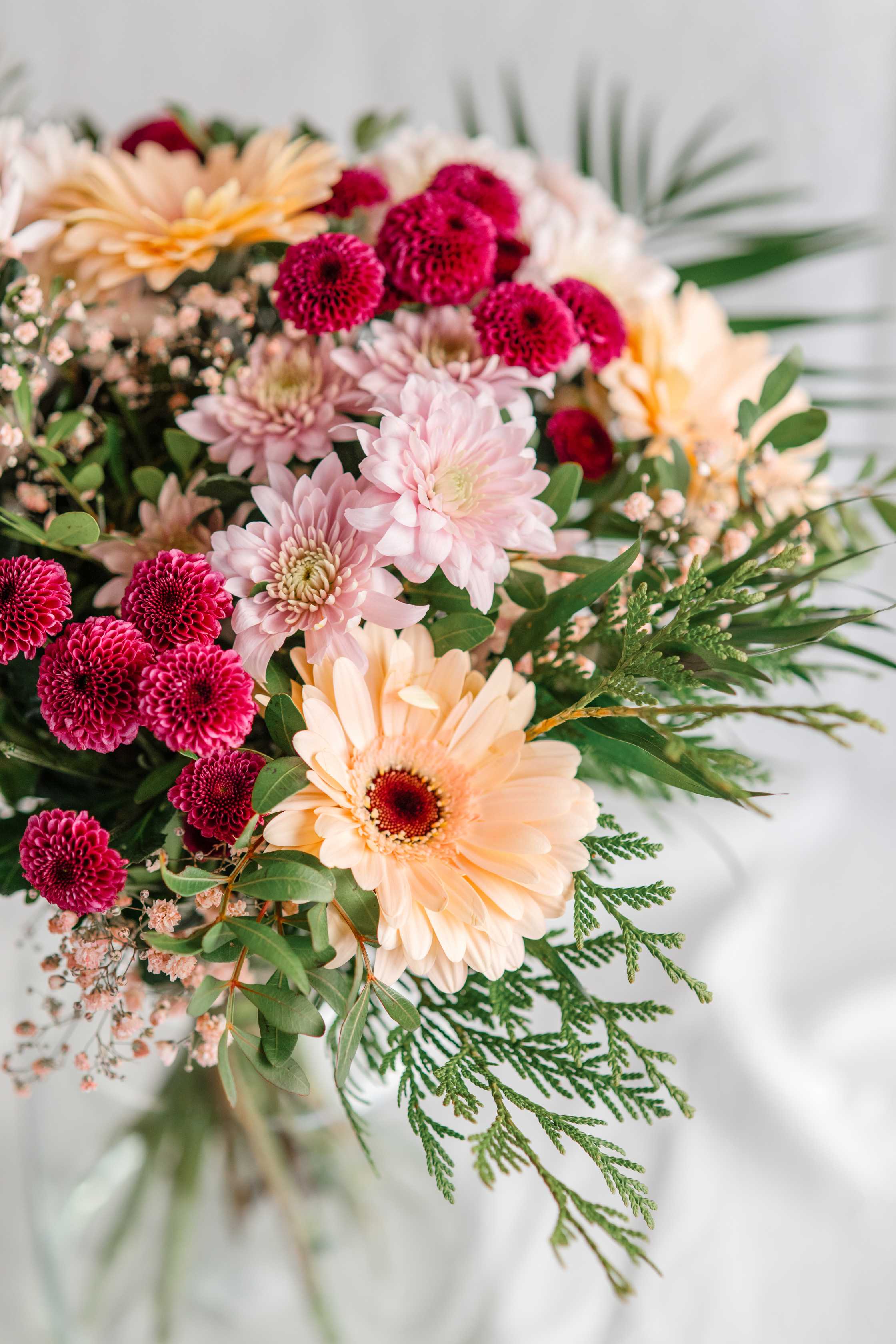 Primer pla de gerbera préssec i crisantems fúcsia i rosa en un ram amb paniculata i verds naturals.