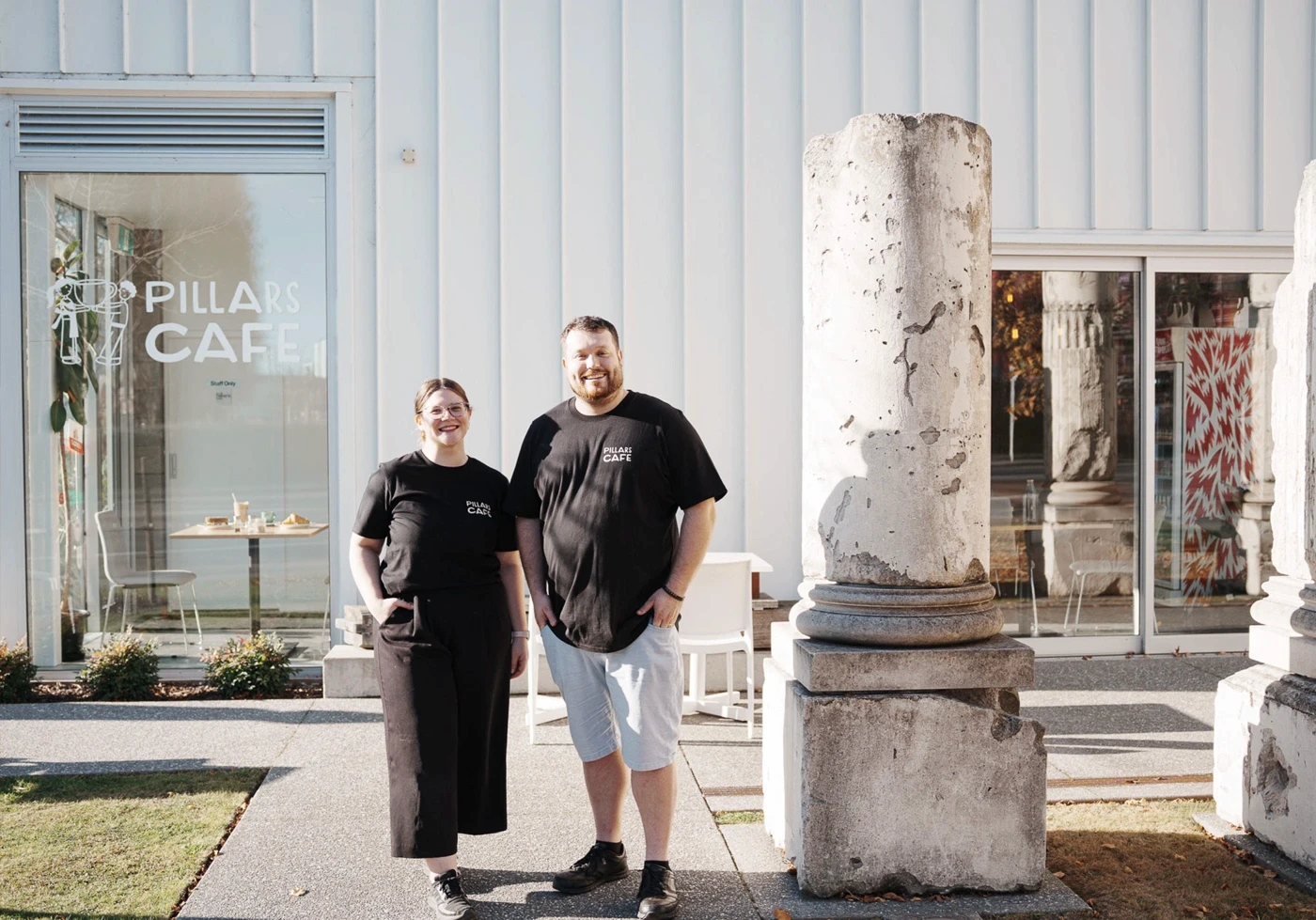 Two Pillars Cafe staff members standing outside the cafe beside historic stone pillars.