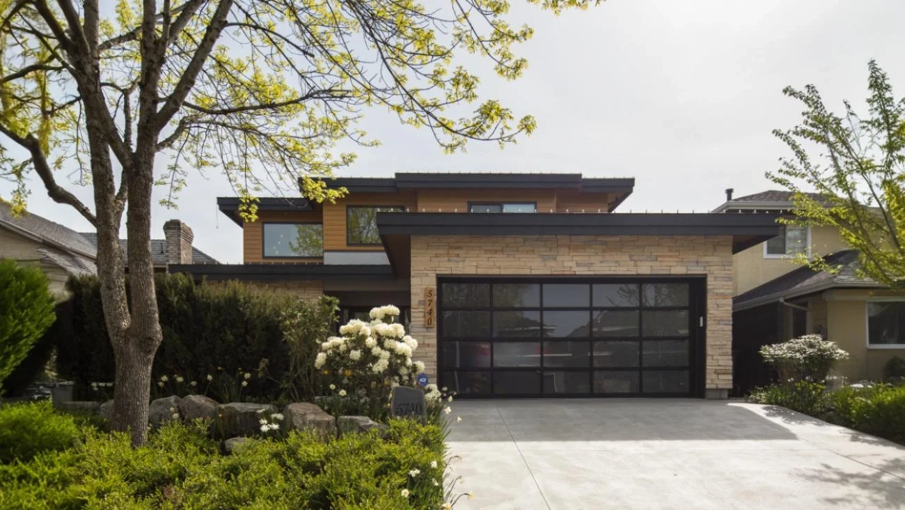 Modern custom home exterior featuring contemporary architecture with horizontal wood siding, natural stone accents, and black-framed garage door in Vancouver