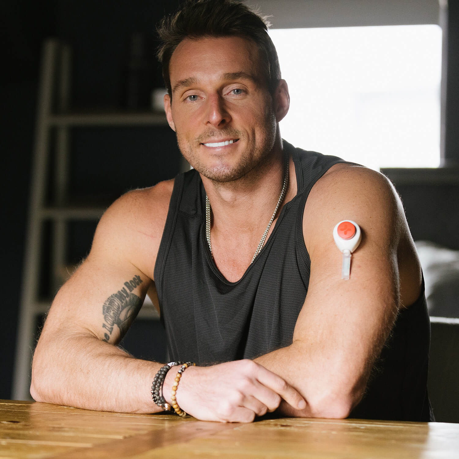Man sitting indoors at a table, pointing at a Rythm Health device attached to his upper arm.