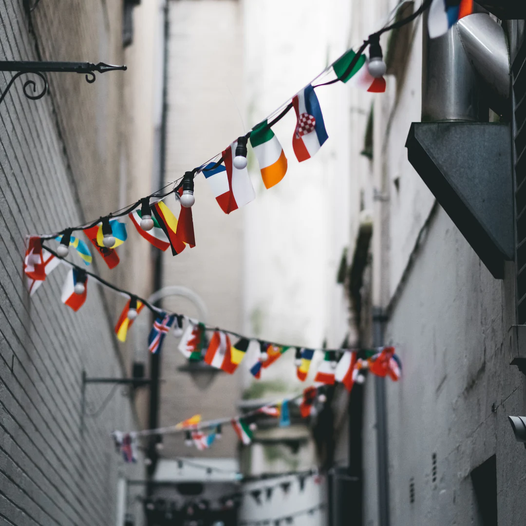 a row of flags on a cord with lights in an alley