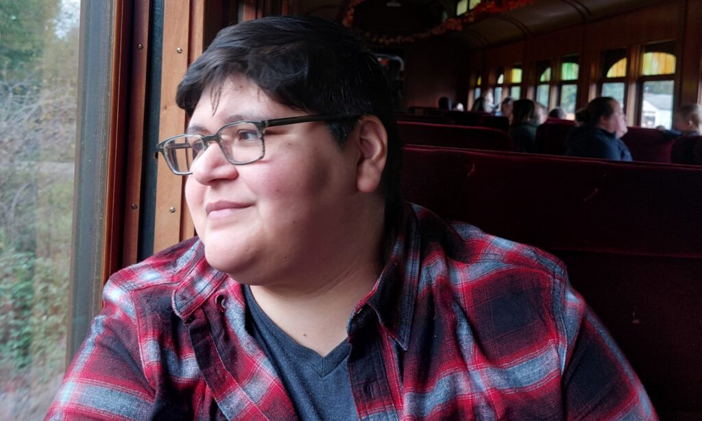 Sarah Mestanza wearing a flannel shirt and looking out the window of a train.