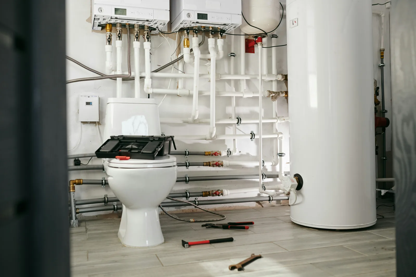 Plumbing utility room with exposed pipes, toilet, and water heater during installation