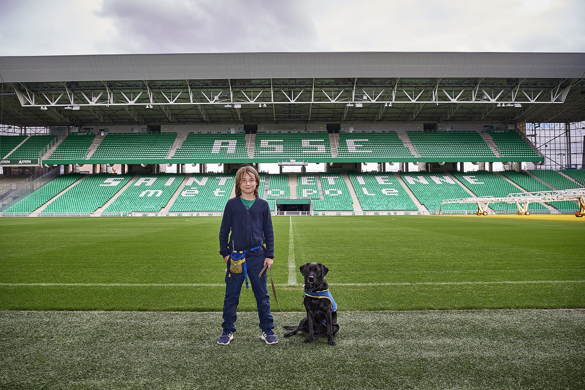 Raphaël accompagné de son chien d’assistance Régate, photographiés par Frédéric Bourcier au stade Geoffroy-Guichard à Saint-Étienne dans le cadre d’un reportage documentaire social pour Handi’Chiens.