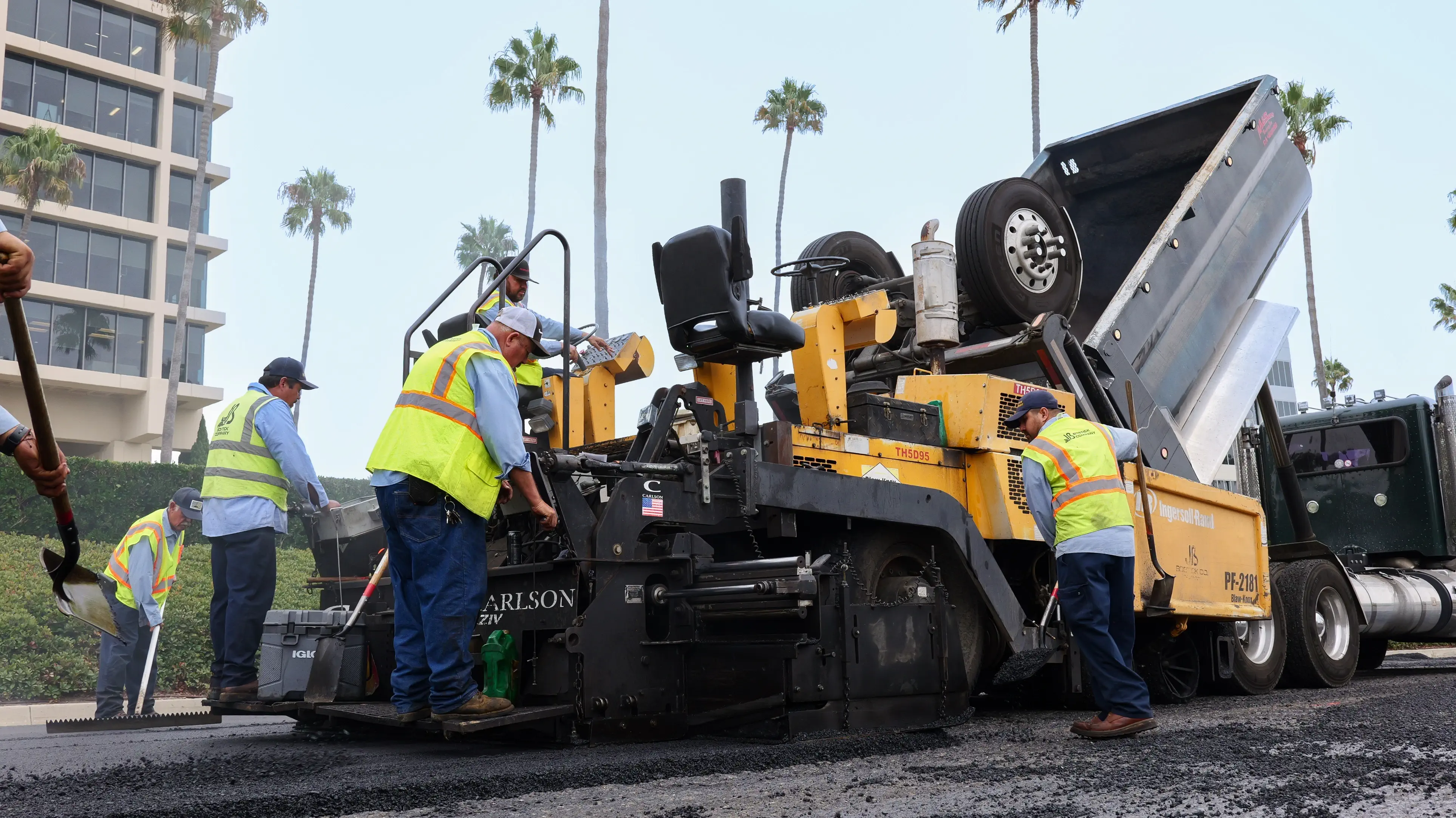 Busy asphalt crew operating paving machine while dumptruck refills asphalt material