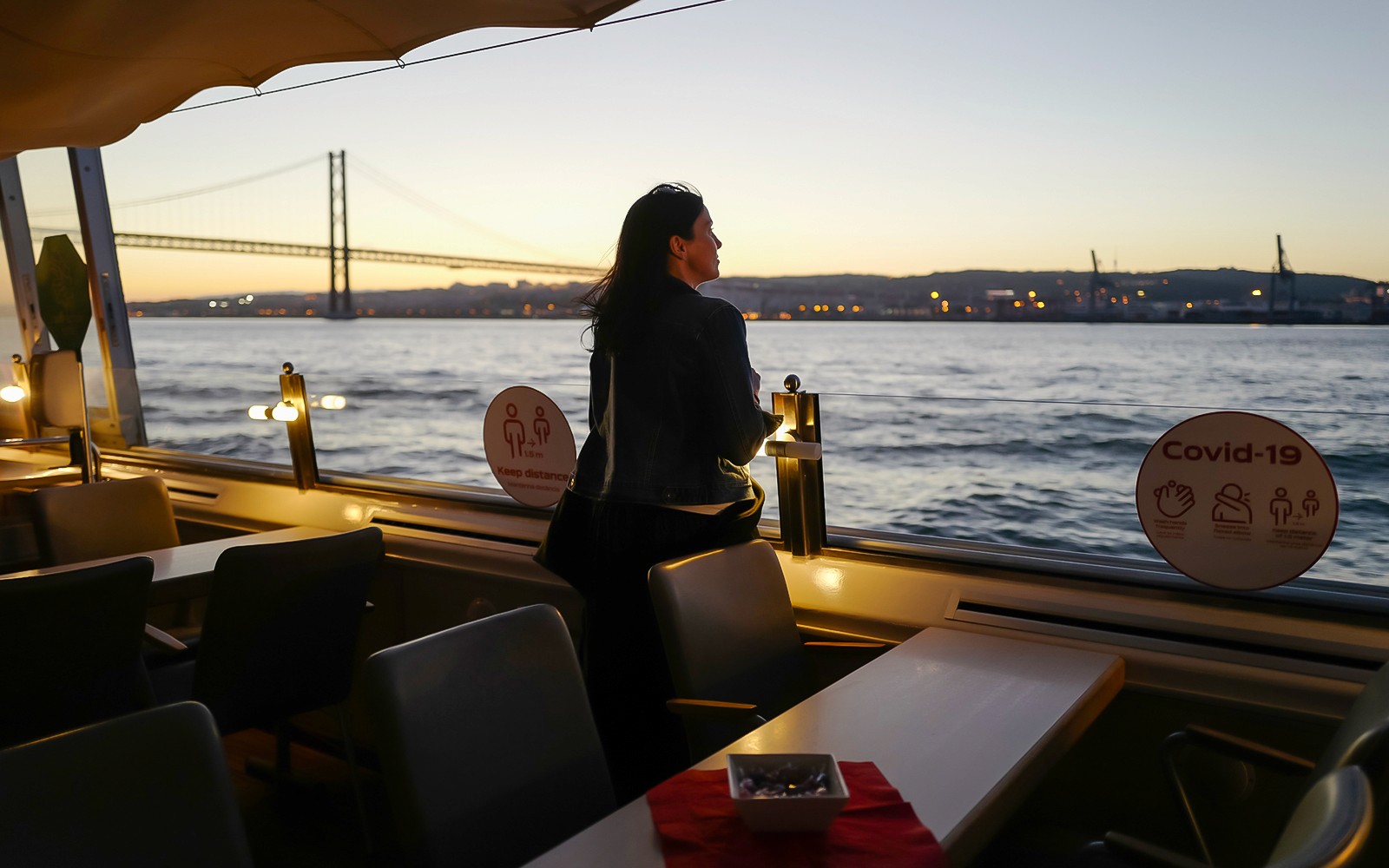 Osoba ciesząca się widokiem zachodu słońca podczas rejsu po rzece Tag w Lizbonie z mostem w tle.