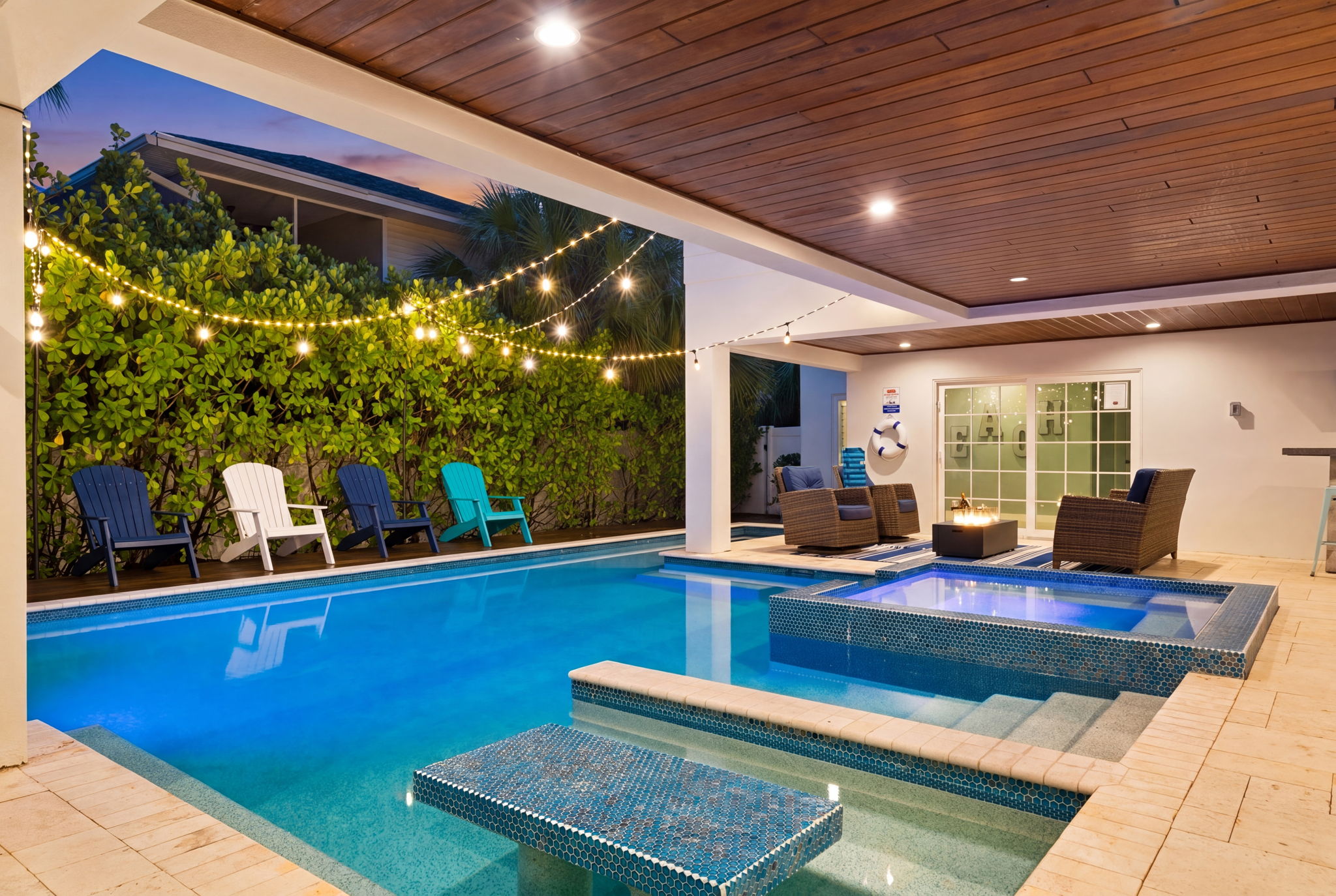 Covered pool and spa at dusk with string lights, Adirondack chairs and a fire table at an Anna Maria Island vacation rental