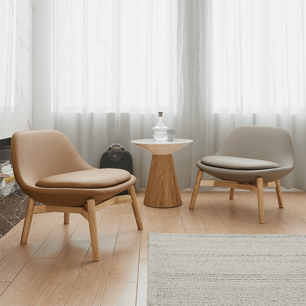 Contemporary accent lounge chairs duo: burnt orange leather and light gray upholstered curved armchairs on solid oak legs, paired with minimalist white top / oak pedestal side table, cozy modern living space with sheer curtains, natural light, wood flooring, and textured rug