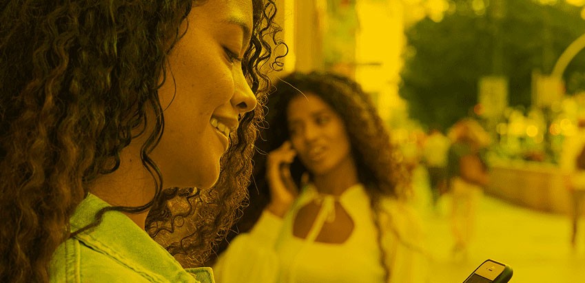 Zwei fröhliche junge Frauen bestellen sich mit ihrem Smartphone ein Taxi.