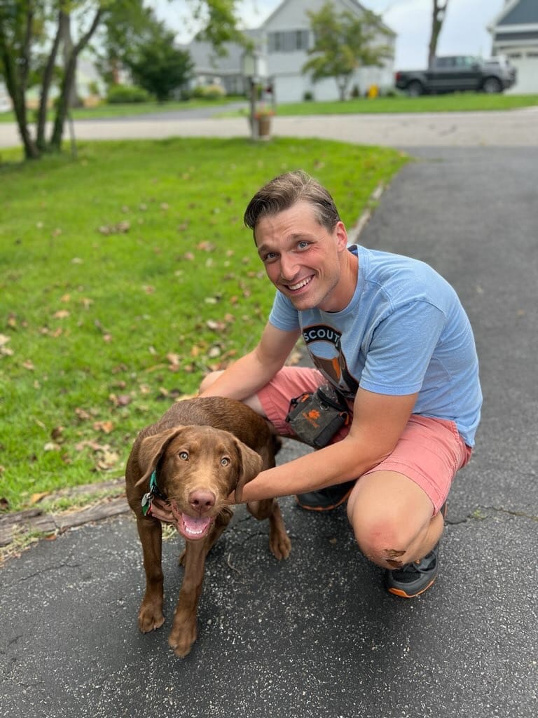 A Pack Leader crouches beside a brown dog during dog training in Maryland