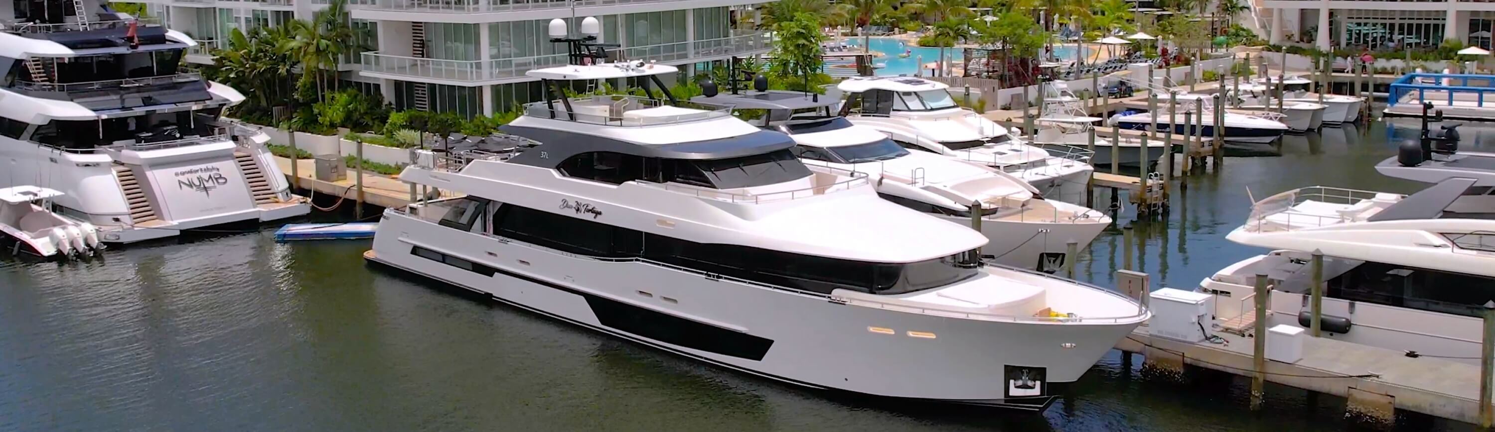 Large white superyacht docked at a luxury marina surrounded by other vessels and waterfront residences.