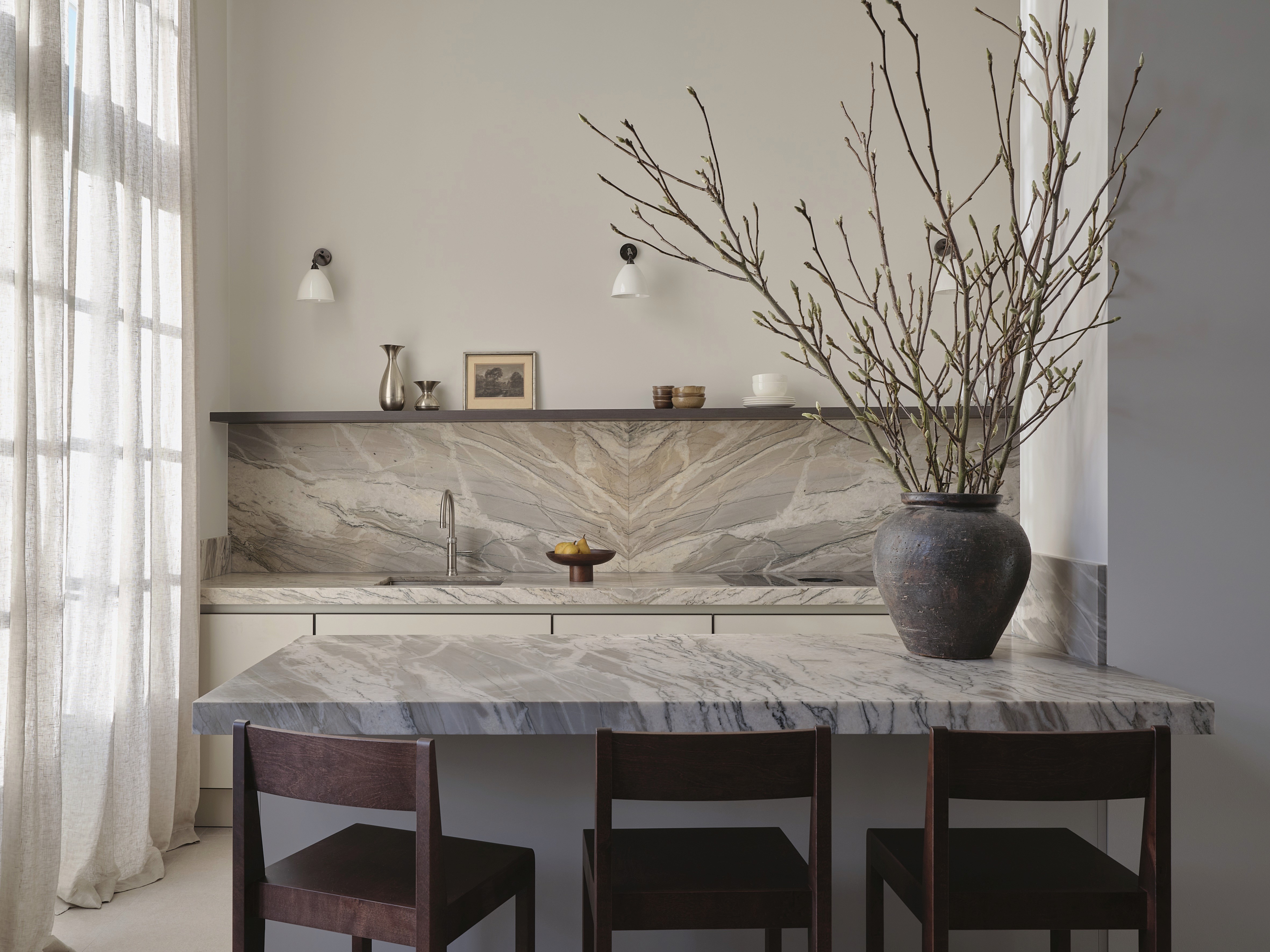 The Residence project - Bespoke kitchen with book-matched quartzite backsplash and island, dark wood bar stools, dark oak open shelving, white ceramic sconces, and vintage vases