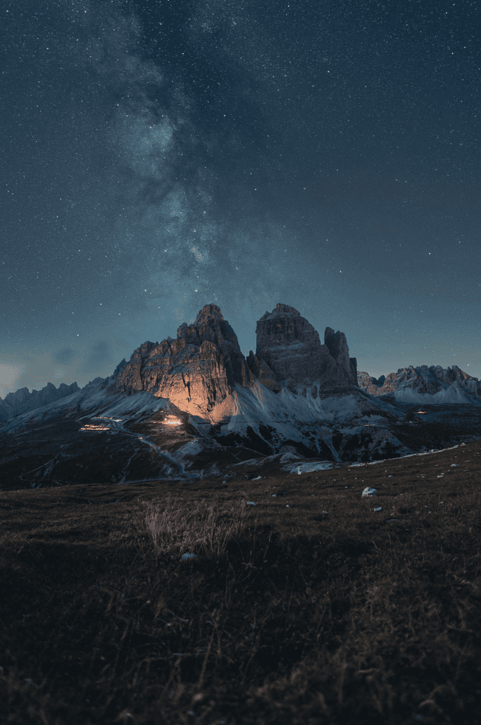 A mountain at the end of a grassy field illuminated by a light on a starry night
