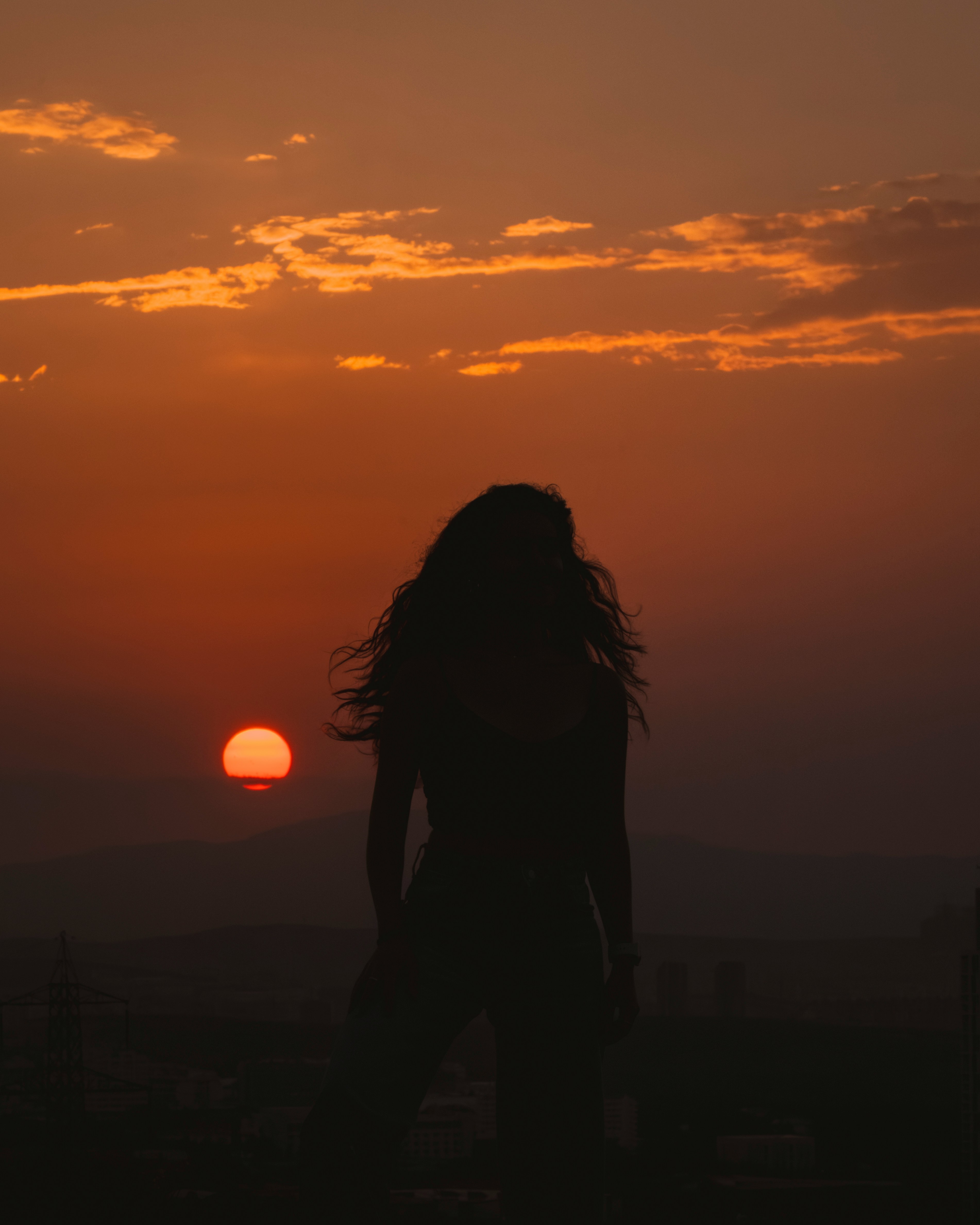 A silhouette of a woman standing in front of a sunset
