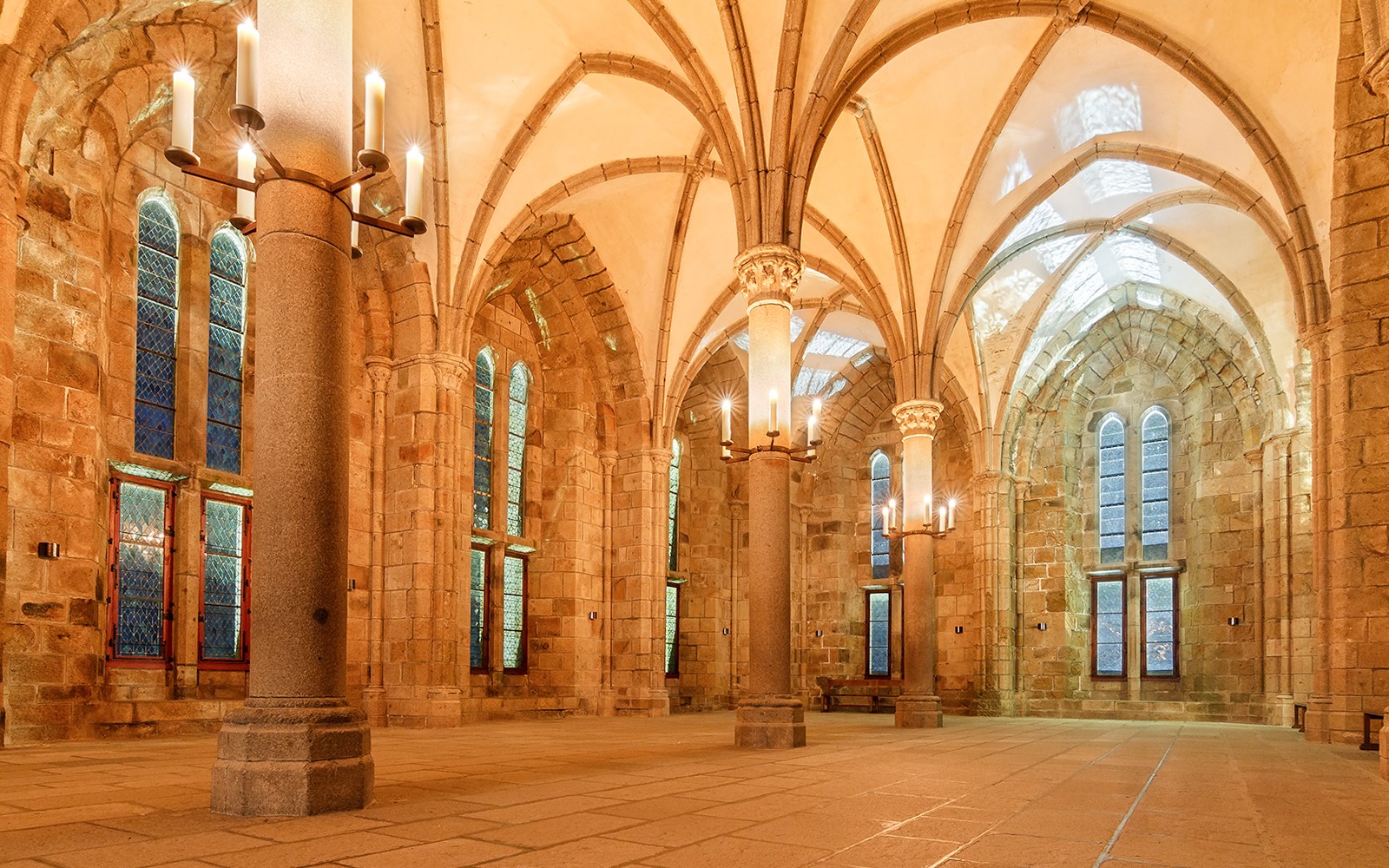 Mont St. Michel Abbey interior with vaulted ceilings and candlelit columns.