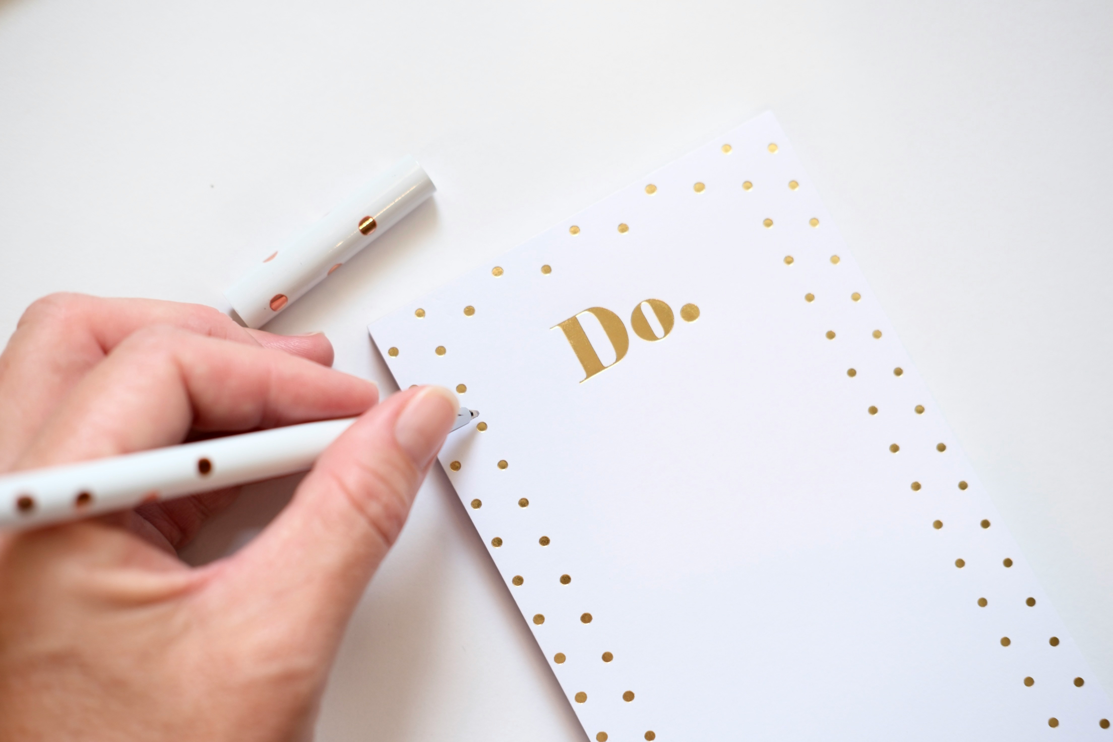 Hand holding a pen over a “DO” to-do list notepad.