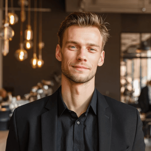 Smiling man in a black suit with blurred office lighting.