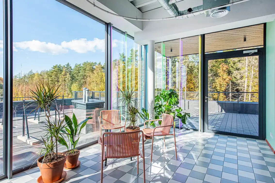 Bright shared lounge and terrace area in student accommodation in Vilnius with seating, plants and large windows.