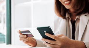 A woman holds a cell phone in one hand and a credit card in the other.