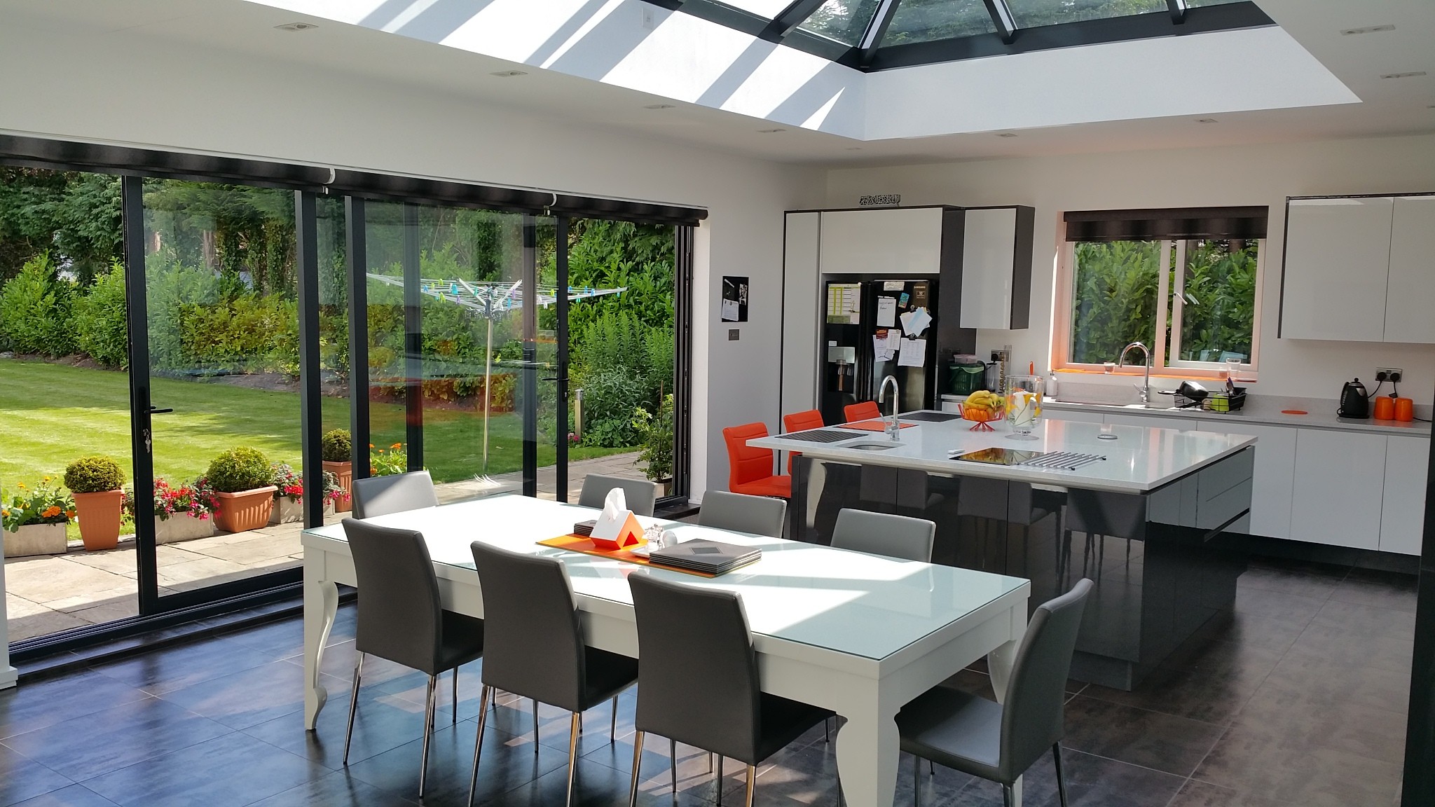 Bright open-plan living area with full-height sliding doors, roof lantern, modern kitchen, and views onto landscaped garden.