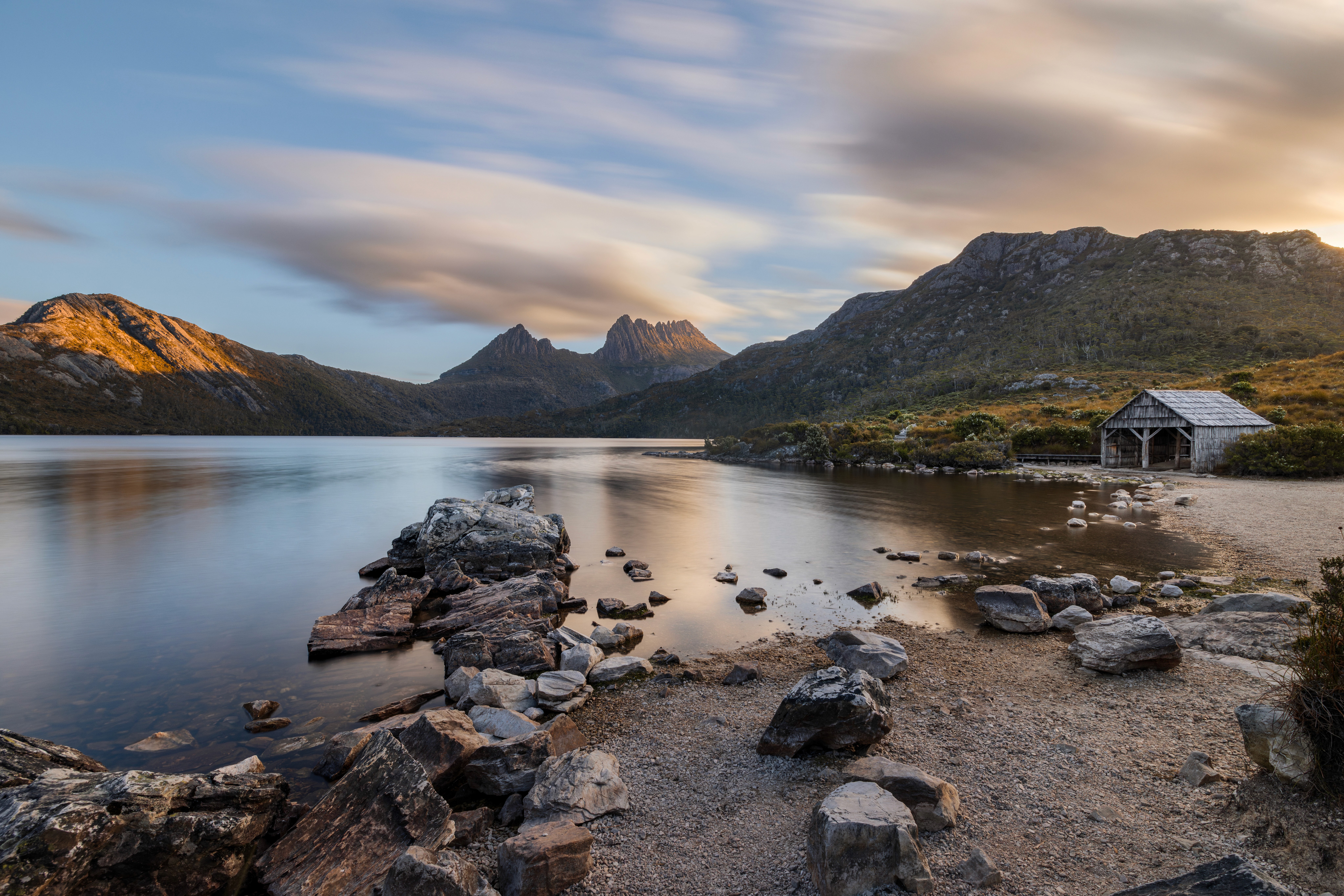 The frame within the frame. By positioning the boatshed at the intersection of the shoreline and the rising mountain slopes, the architecture provides a human scale to the vast, atmospheric composition of the park.