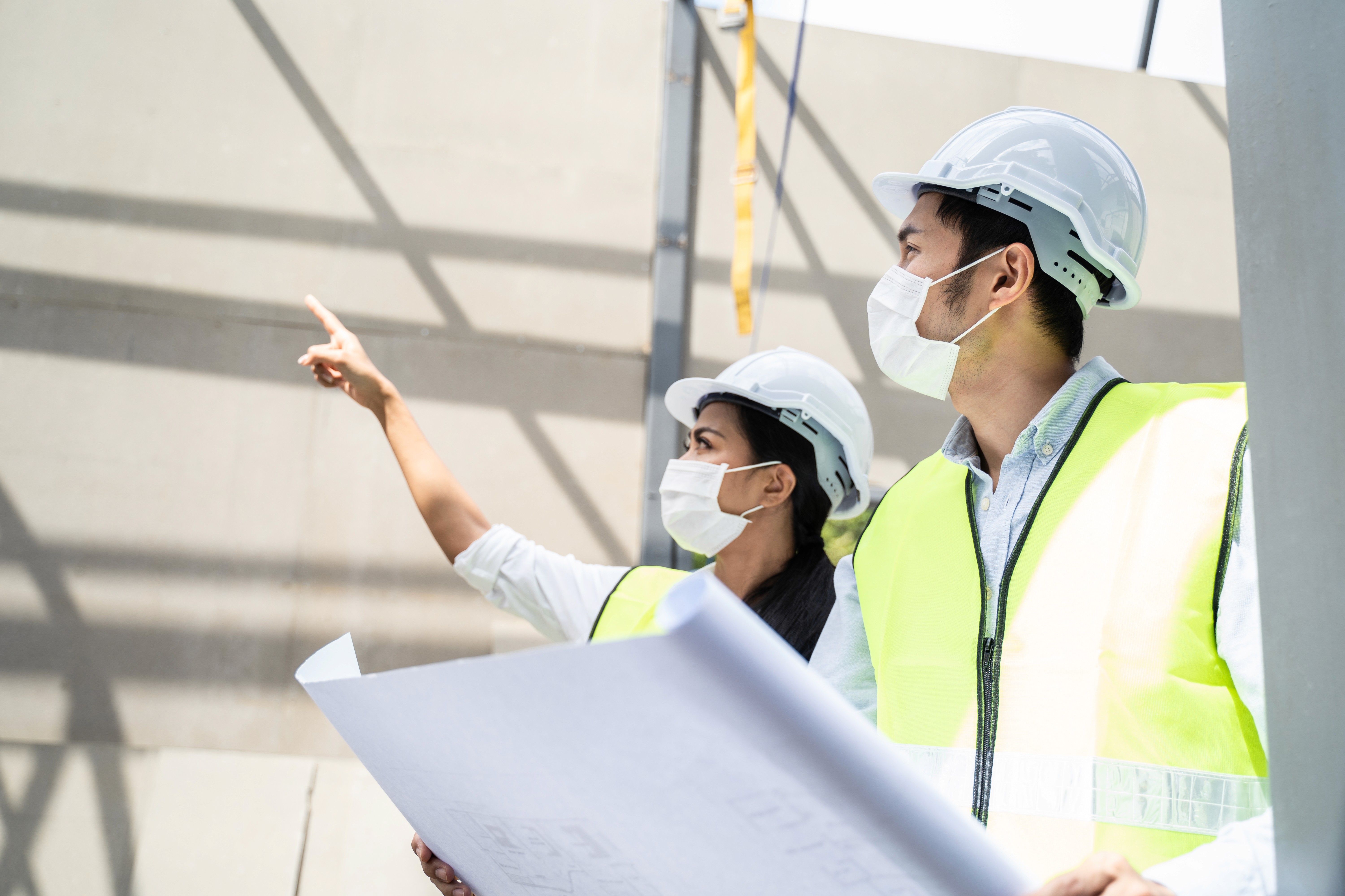 戴安全帽與反光衣的專業人員於建築地盤查看圖則，提供工程保險及勞保風險管理與顧問服務。