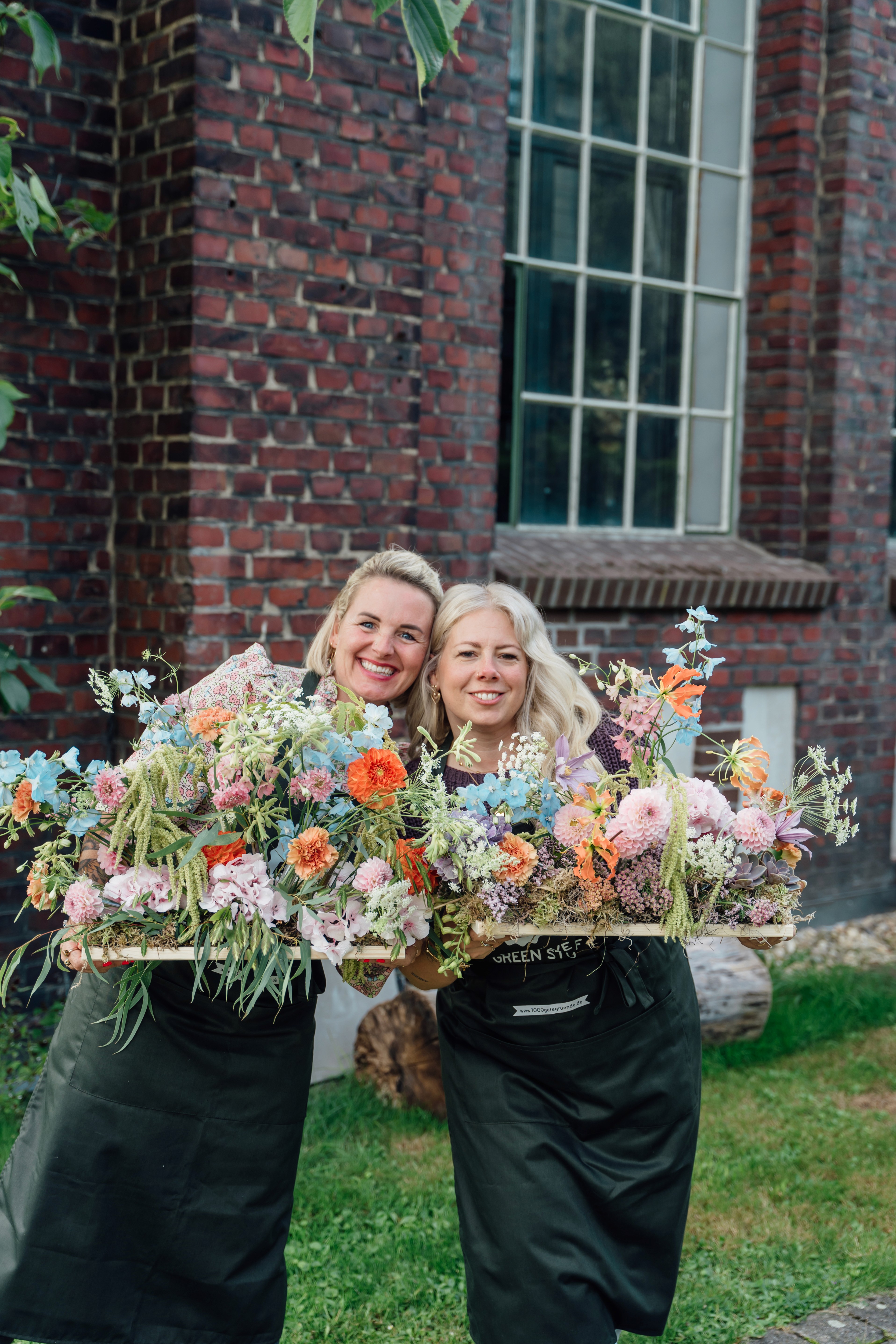 Zwei Frauen präsentieren florale Gestecke bei einem Blumen-Workshop mit 1000 gute Gründe.
