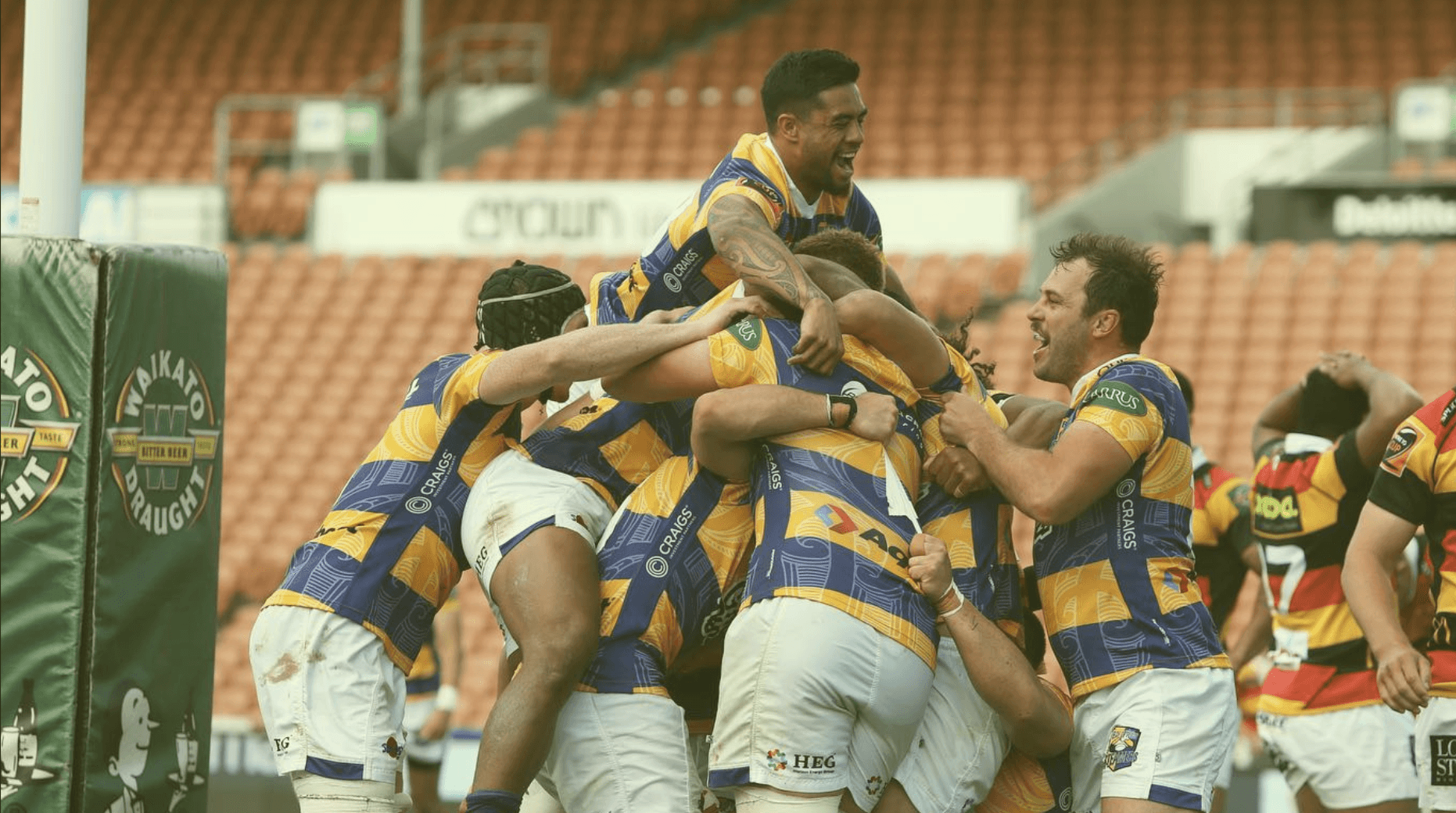 A smiling woman with curly hair is posing in a warmly lit indoor setting. She wears a dark-colored shirt.