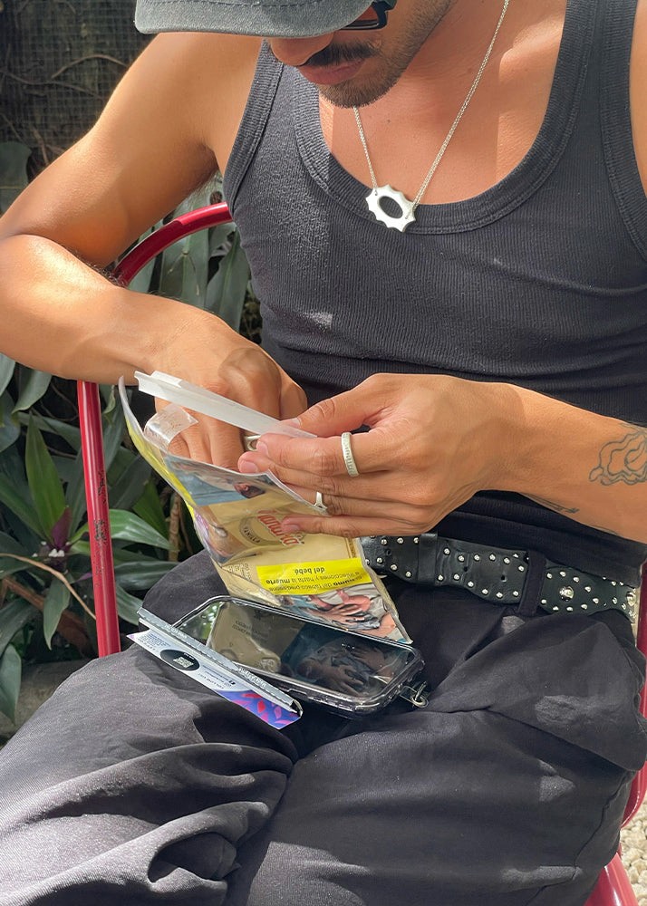 Man wearing silver jewelry and a silver pendant rolling a cigarette