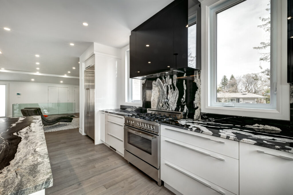 Bright open-concept kitchen and dining area with black and white marble waterfall island, sleek white cabinetry, and glass staircase, showcasing B&Y Reno Corp’s custom kitchen remodeling in a modern luxury home.