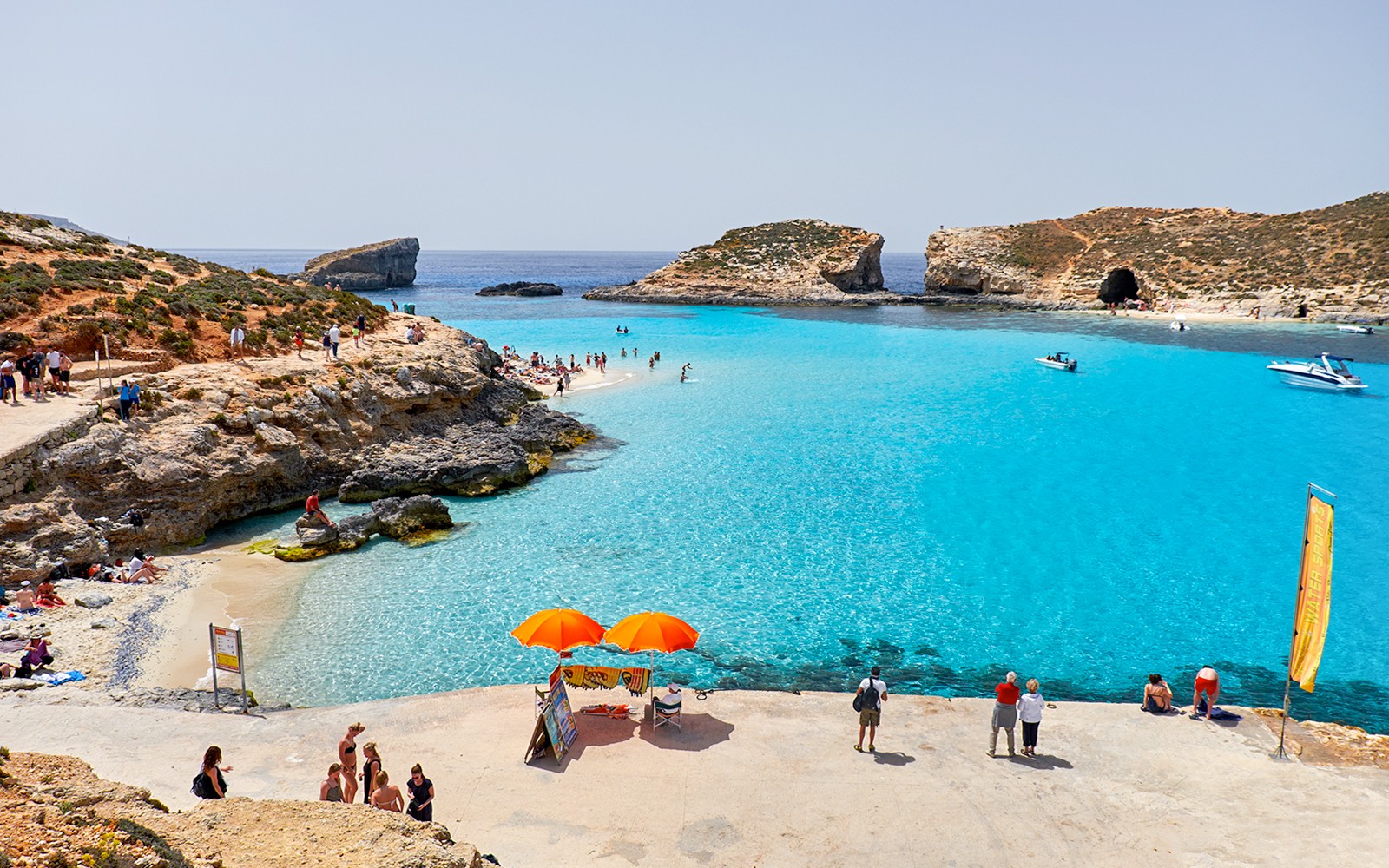 Visitors enjoying the clear waters of Blue Lagoon, Malta with boats and rocky cliffs in the background.