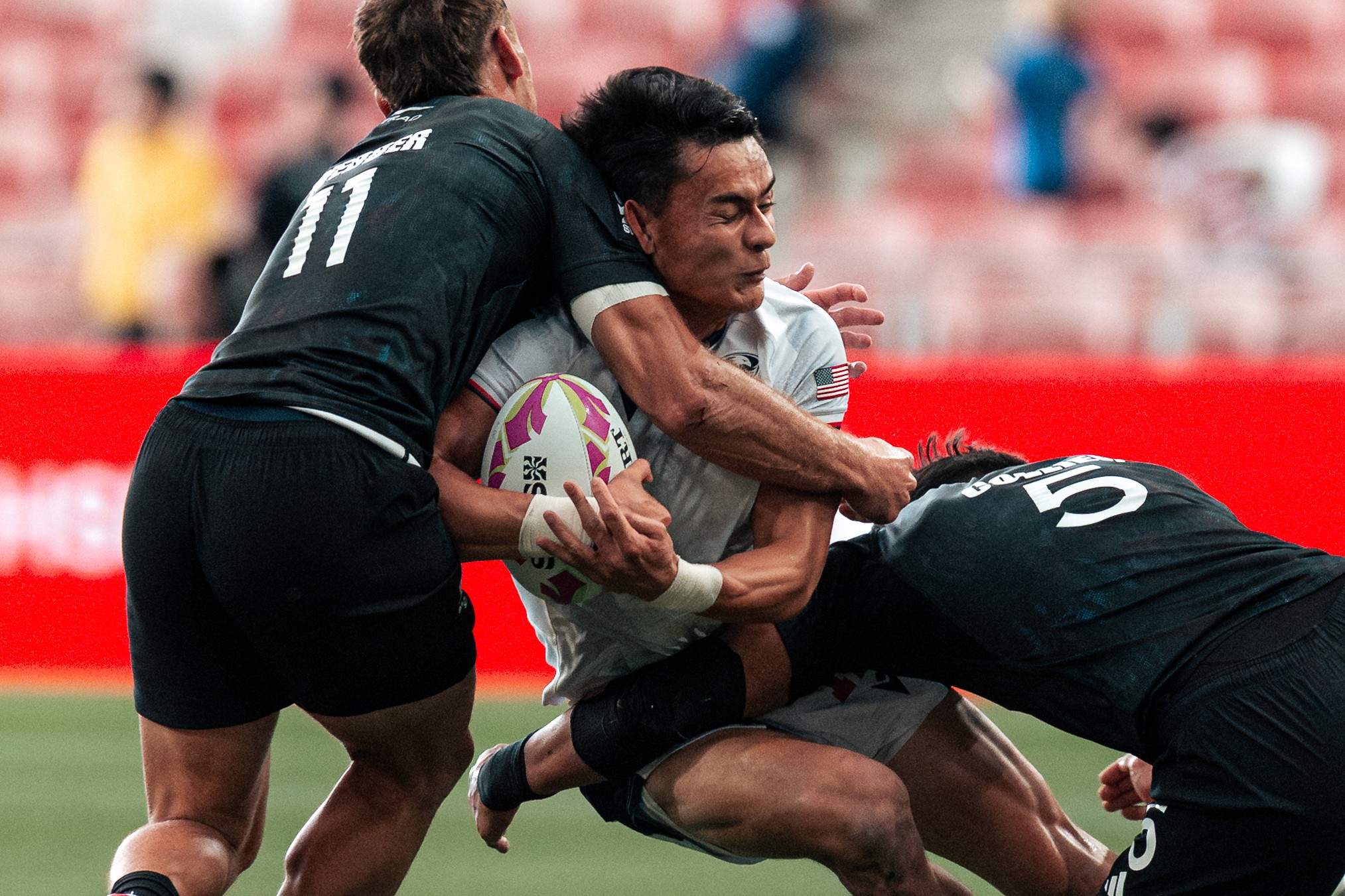 Lucas Lacamp of USA tussles against 2 New Zealand All Blacks players during a match at the HSBC SVNS Singapore 2025