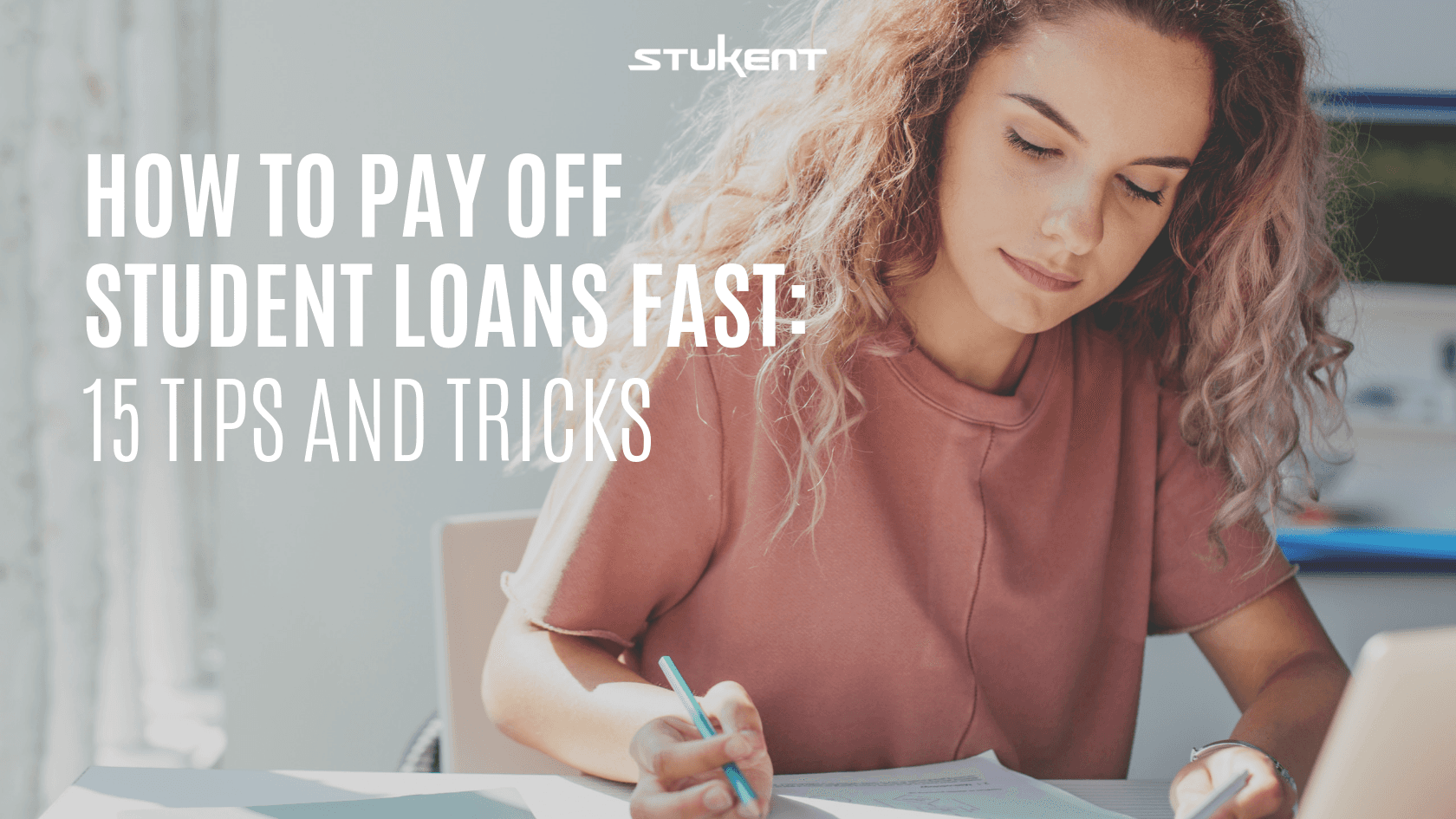 Young woman writes in a notebook while using a laptop. Text reads: “How to Pay Off Student Loans Fast: 15 Tips and Tricks.” The Stukent logo appears above the text.