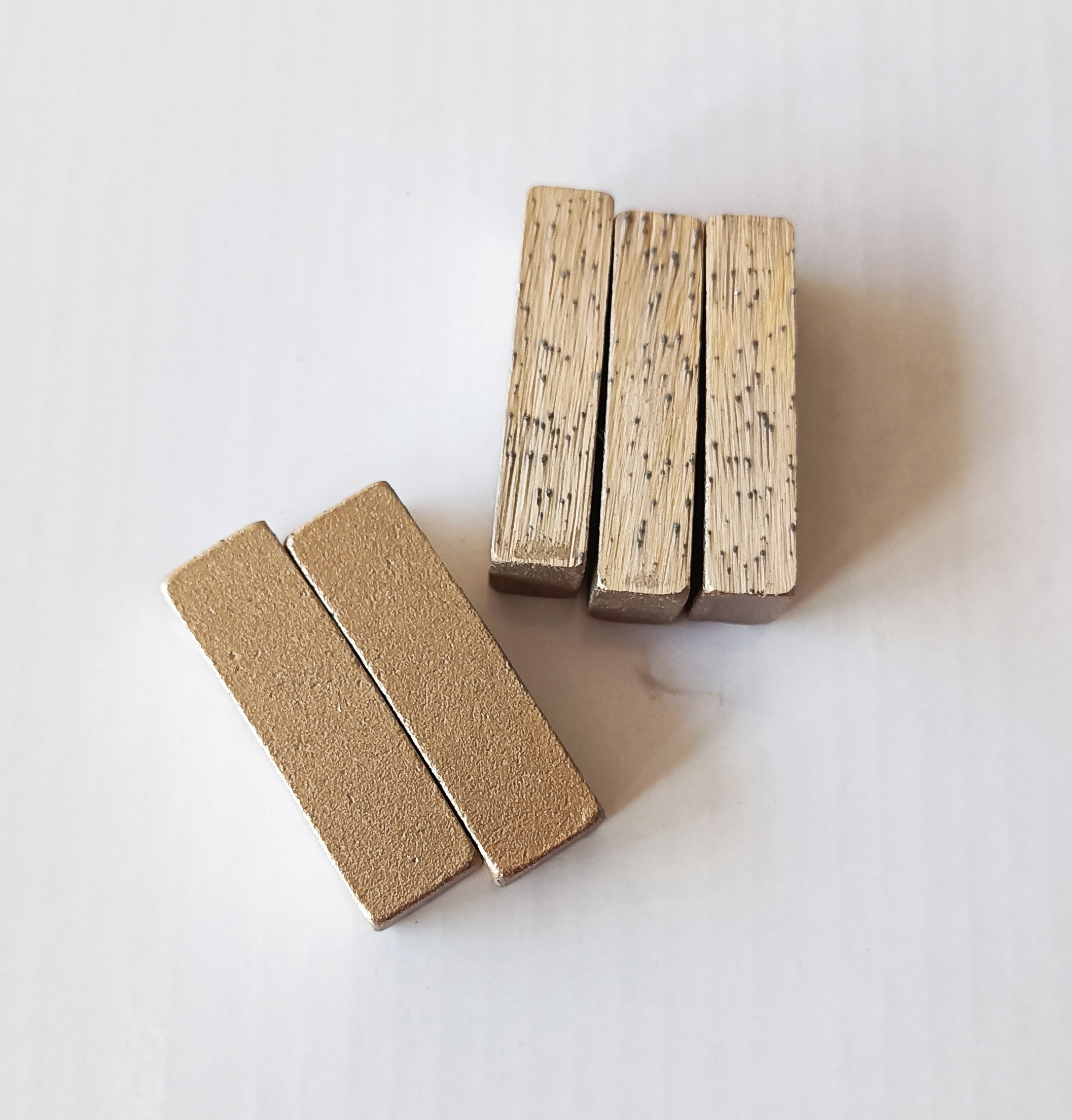 Five pieces of diamond segment for marble cutting on the white background plate, the left two pieces of slightly curved, the surface is regular slightly rough, the right three pieces of the display is the side, the bare diamond broken after the cut surface, from the cut surface can be seen that diamond distribution is uniform, the cutter head surface have a light metallic luster