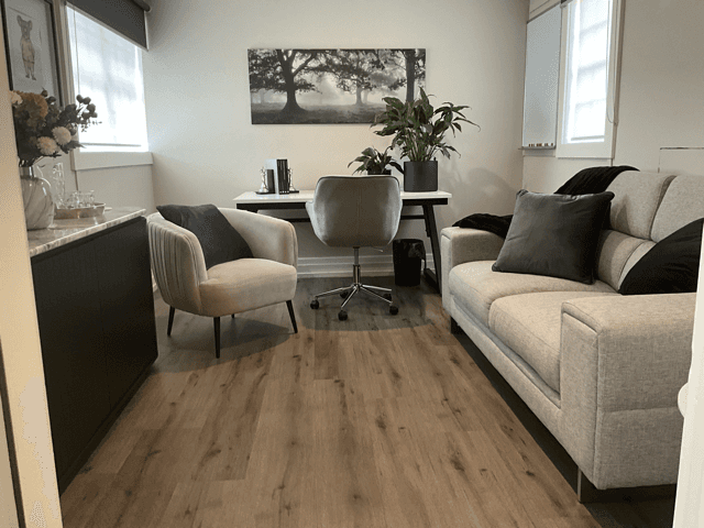 Cozy waiting room with gray chairs, a coffee table, plants, and a window letting in natural light.