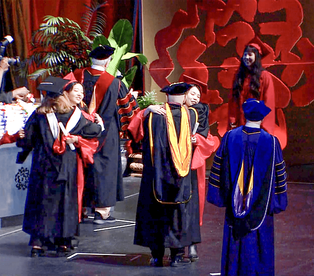 students on stage hugging professors at graduation