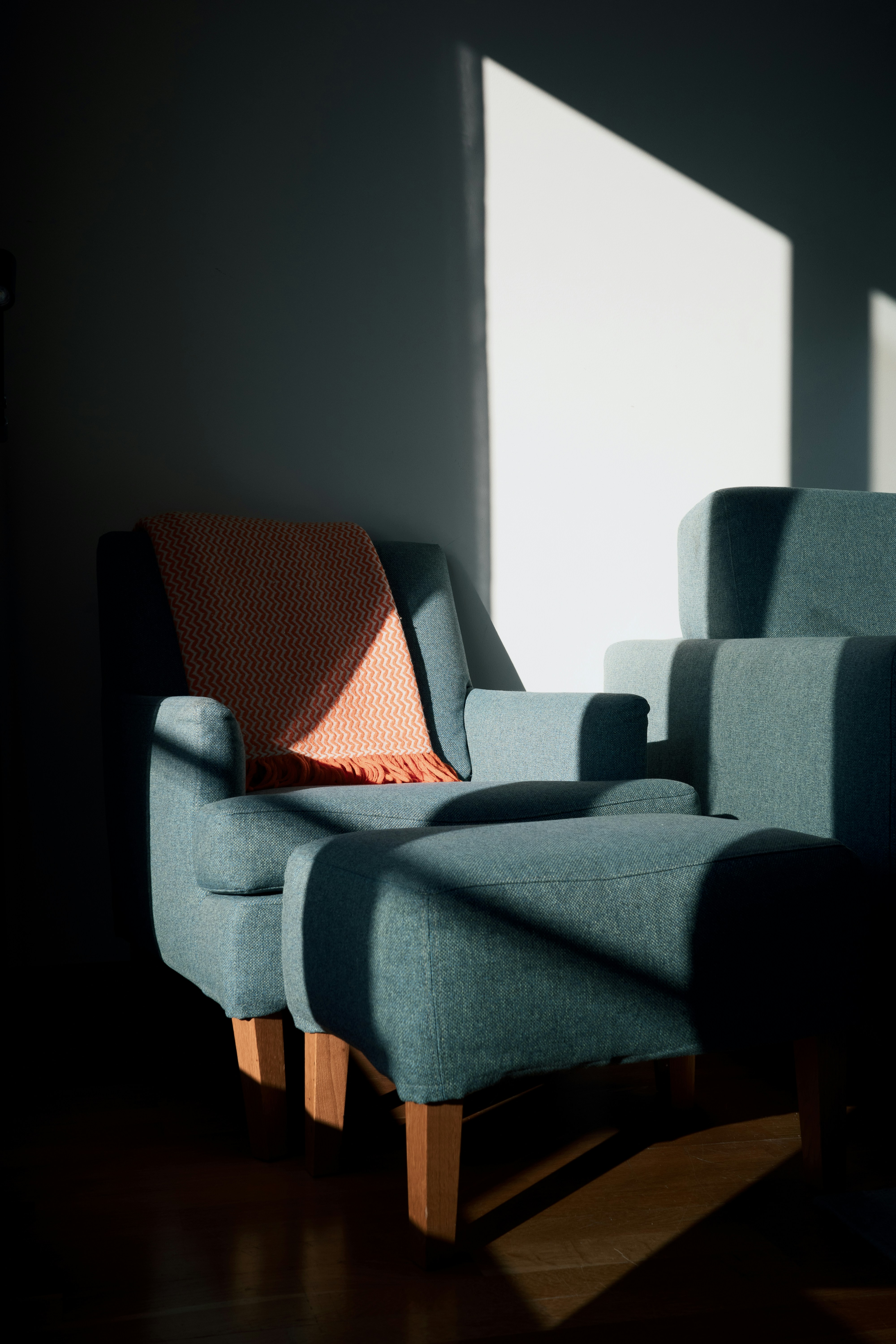 An armchair and ottoman with a blanket in sunlight.