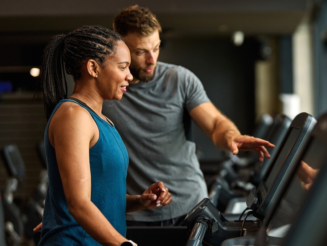fitness instructor giving a woman walking help lose weight on a treadmill at the gym