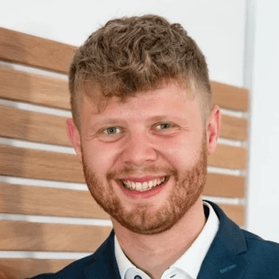 Rupert Zeltsperger steht im Anzug vor einer Wand und lächelt