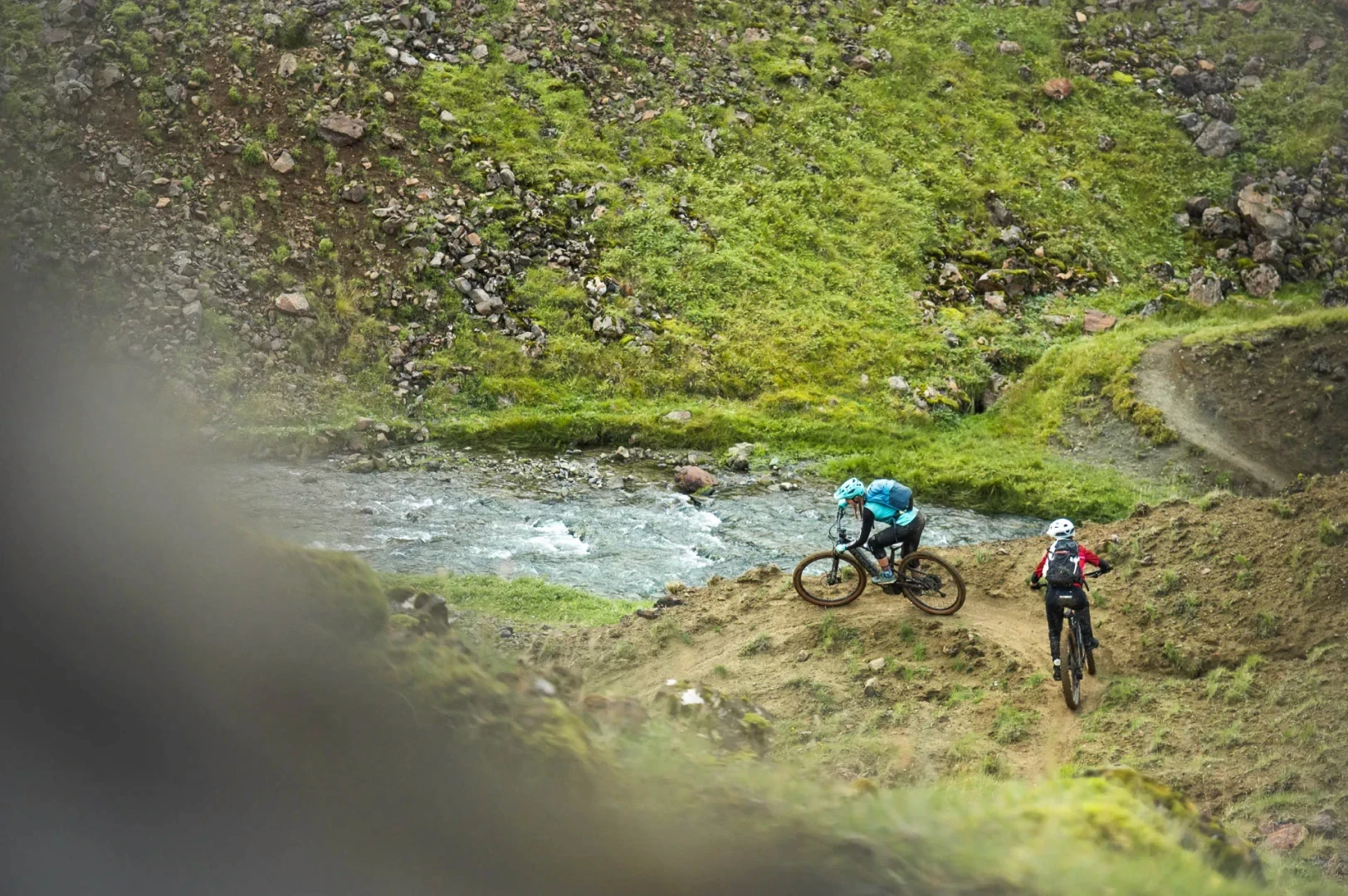 two women ride mtb in geothermal area green lush and river