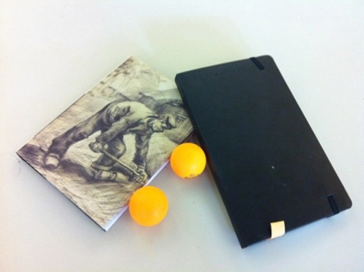 a notebook with an illustration of a working man, a black back cover of a notebook, and two table-tennis yellow balls