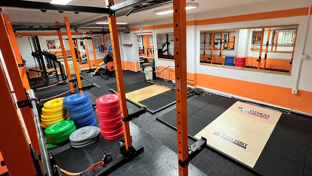 Silová zóna posilovny — squat rack, barevné kotouče a olympijská platforma