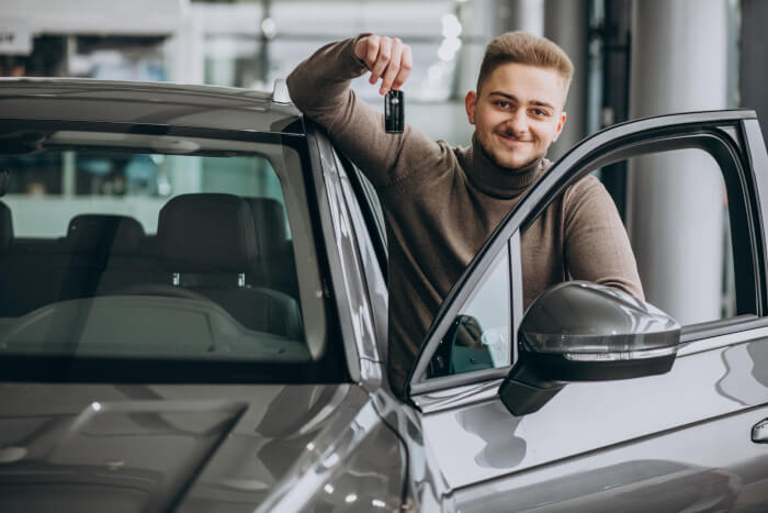 Șofer zâmbind lângă mașină – protecție obligatorie RCA oferită prin BIXMA Asigurări.