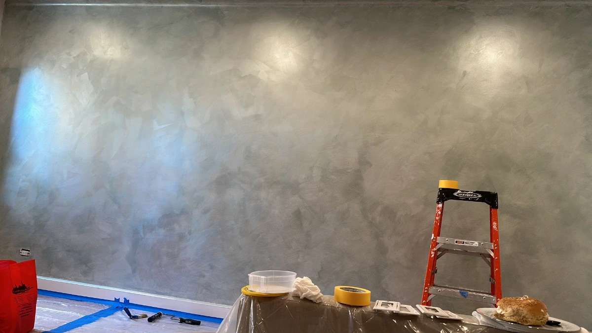 Venetian plaster feature wall in a soft gray finish with a subtle, hand-applied texture, illuminated by overhead lighting in a modern interior space.