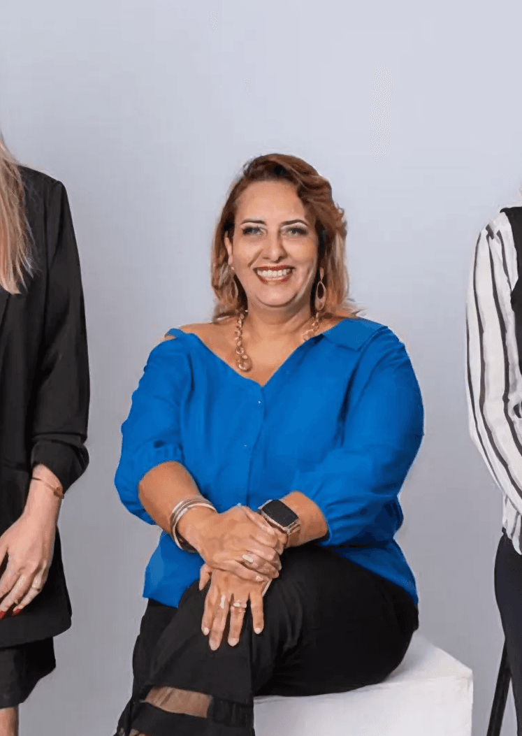Woman sitting in sunlight with eyes closed, wearing relaxed neutral clothing in a peaceful setting.