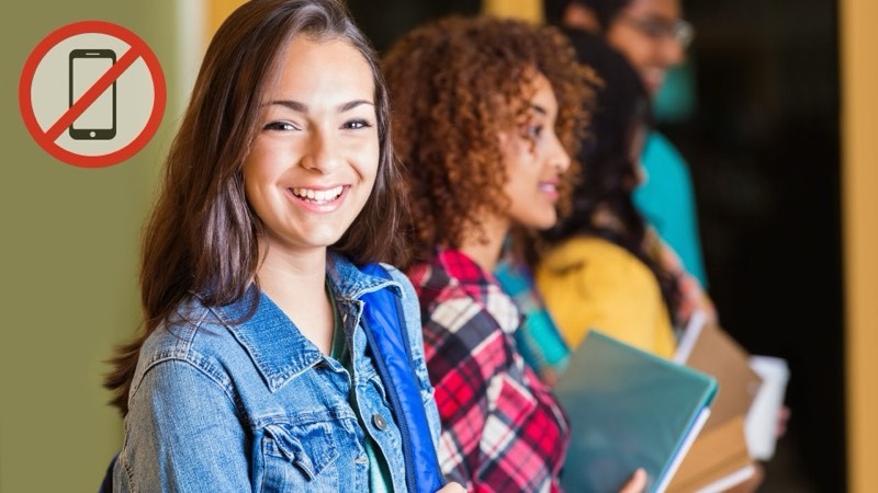 students smiling in hall with no phone policy sign
