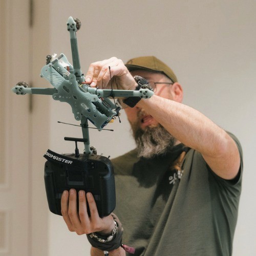 Man attaching a controller to a camouflage-painted FPV drone frame