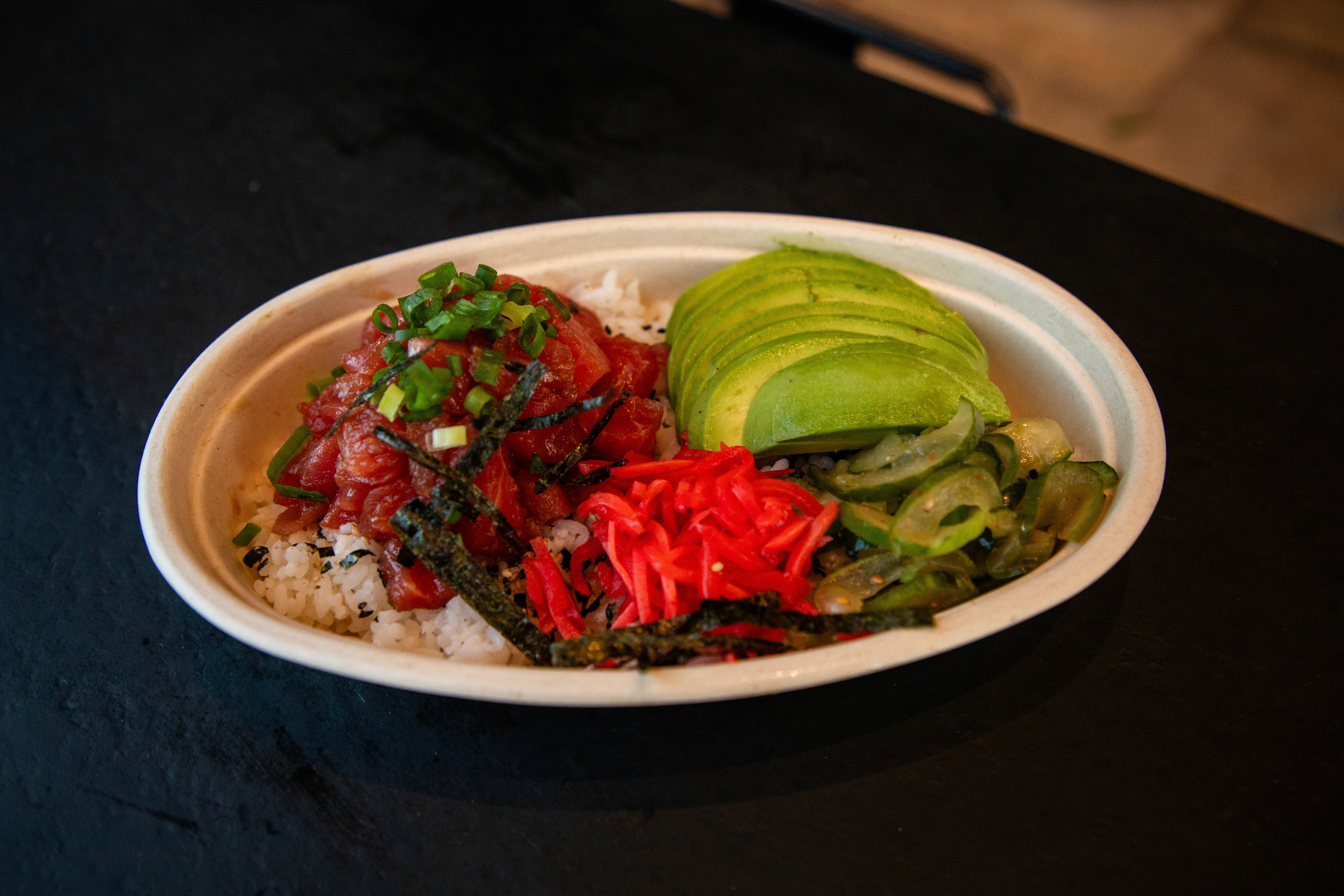 A close-up shot of a fork twirling strands of creamy white pasta, possibly carbonara or cacio e pepe, heavily garnished with dark black pepper or truffle shavings, against a stark white background.