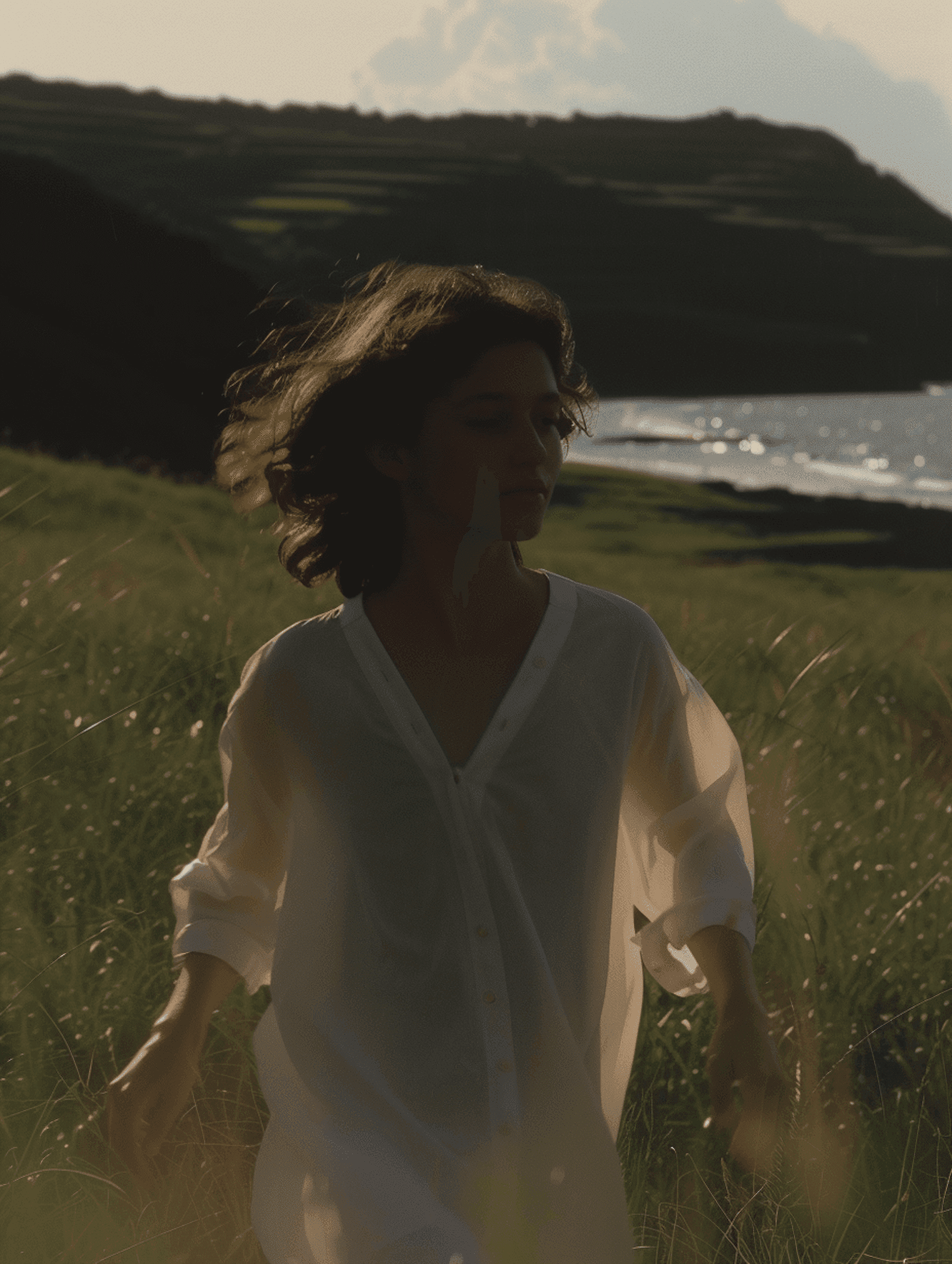 Person in white shirt walking through a green landscape near the sea