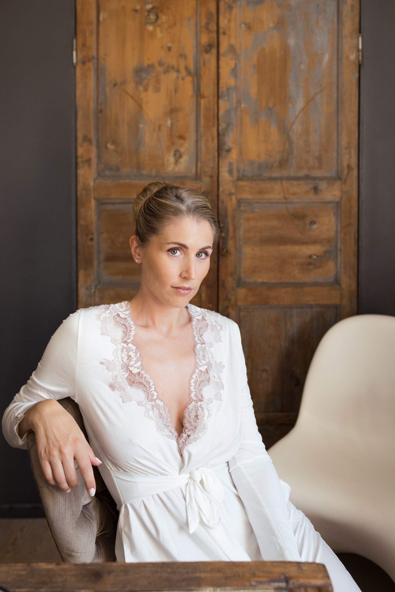 Sposa in abito bianco con pizzo ricamato a Villa Malenchini, seduta accanto a porta in legno antico, reportage matrimoniale